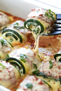 a spoon full of food being lifted from a casserole dish with zucchini and spinach