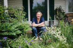 a woman is sitting on the steps in front of her house surrounded by plants and flowers