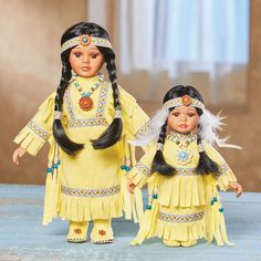 two dolls dressed in native american clothing and headdress, standing next to each other