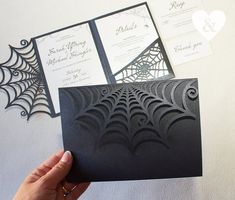 a person holding up some black paper with spider webs on it and the inside of their wedding stationery