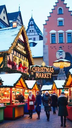 people are walking through an outdoor market with christmas decorations and lights on the buildings in the background