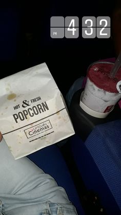 a person sitting in a seat holding a paper bag filled with popcorn and a drink