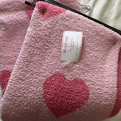 two pink towels with hearts on them sitting on top of a white bed next to a black zippered bag