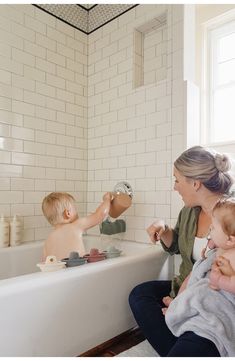 a woman and two children in a bathtub with soap on the faucet