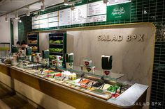 the salad box has many different types of food on display at it's counter