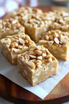 some kind of dessert sitting on top of a wooden cutting board with white paper and nuts