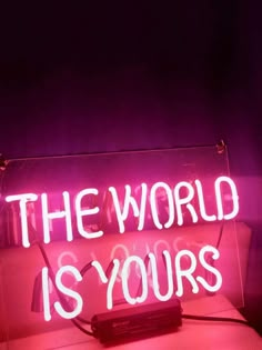 a neon sign that says the world is yours in white letters on a pink couch