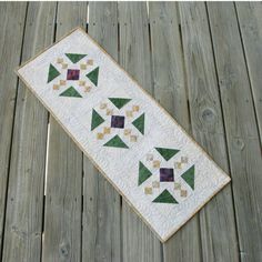 a quilted table runner with green and brown triangles on it, sitting on a wooden deck