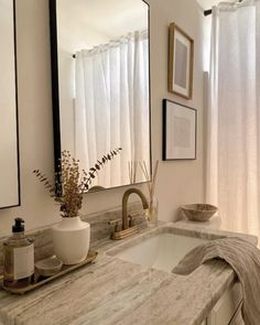 a bathroom sink under a large mirror next to a window with white drapes on it