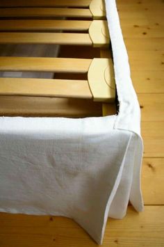 a wooden bed frame with white linen on it and wood slats in the background