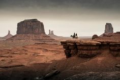 two people ride horses through the desert on a cloudy day in monument national park, utah