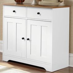 a white cabinet with two drawers and plates on top in a room next to a wall