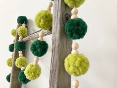 green and white pom - poms hang from a wooden pole on the wall