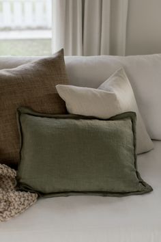 three pillows on a white couch in front of a window