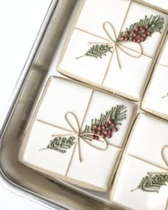 four square cookies decorated with holly and red berries in a tin on a white table