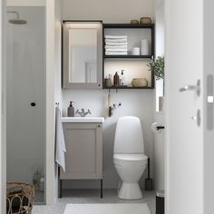 a white toilet sitting in a bathroom next to a sink and shower stall with towels on the shelves