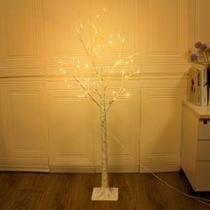 a lighted tree in the corner of a room with white walls and wood flooring