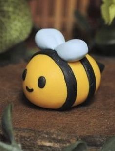 a small yellow and black toy bee sitting on top of a wooden table next to plants