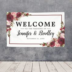 a welcome sign hanging from the side of a wall with flowers and leaves on it