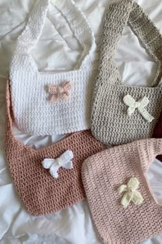 four crocheted purses on a bed with white sheets and pink, red, blue, and beige colors