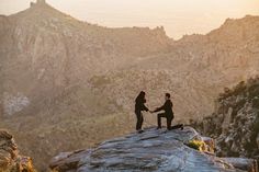 two people standing on top of a mountain holding hands and shaking hands with each other