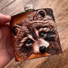 a hand holding a flask with a drawing of a raccoon on it