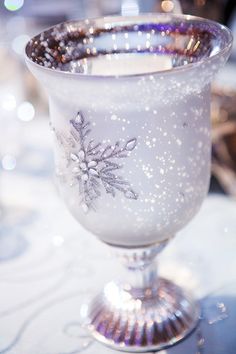 a glass filled with liquid sitting on top of a white table covered in snowflakes