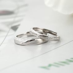 two wedding rings sitting on top of a table next to a white flower and glass vase