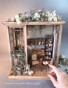 a hand is holding up a doll house with flowers on the top and shelves below