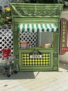 a green and yellow food cart sitting on top of a wooden floor next to a white fence