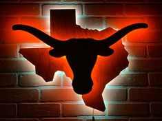 the texas longhorns logo is lit up on a brick wall in front of an orange light