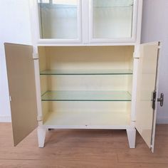 a white cabinet with glass doors and shelves on the bottom, in front of a wall