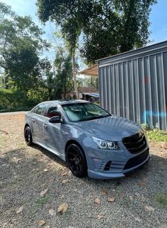 a silver car parked in front of a metal building next to a tree and fence