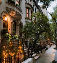 a city street lined with tall buildings covered in trees and bushes at night, lit by lights on the windows