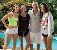 three women and a man standing next to each other in front of a swimming pool