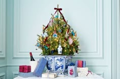 a small christmas tree in a blue and white vase surrounded by presents on a table