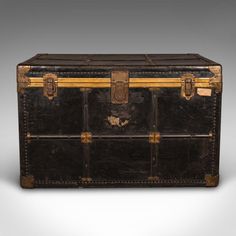 an antique trunk with gold trimmings on the top and bottom, sitting against a gray background