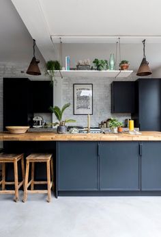 a kitchen with blue cabinets and wooden stools next to a counter topped with potted plants