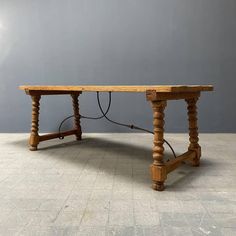 an old wooden table sitting on top of a tile floor next to a gray wall