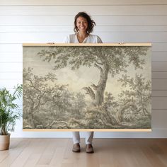 a woman holding up a painting with trees on it