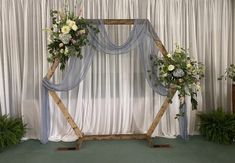 an arch decorated with flowers and greenery in front of a white curtained backdrop