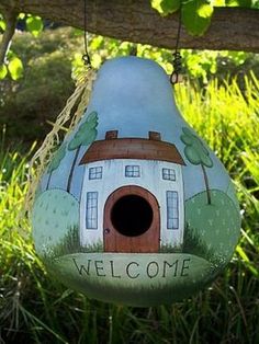 a birdhouse hanging from a tree branch with the words welcome painted on it's side