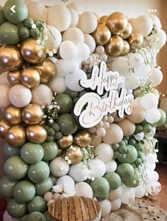 a birthday party with balloons and greenery on the wall in gold, white and green colors