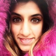 a woman with long hair wearing a pink fur coat and smiling at the camera while looking into the camera