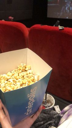 a person is holding a box of popcorn in front of the screen at a movie theater