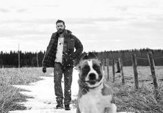 a man and his dog walking down a path in the snow near a fenced in field