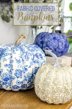 three fabric covered pumpkins sitting on top of a wooden table next to blue and white vases