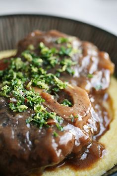 meat and gravy on top of mashed potatoes in a black plate with garnishes