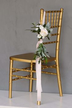 a gold chair with white flowers and greenery tied to the back, against a gray wall