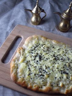 a pizza sitting on top of a wooden cutting board next to two silver teapots